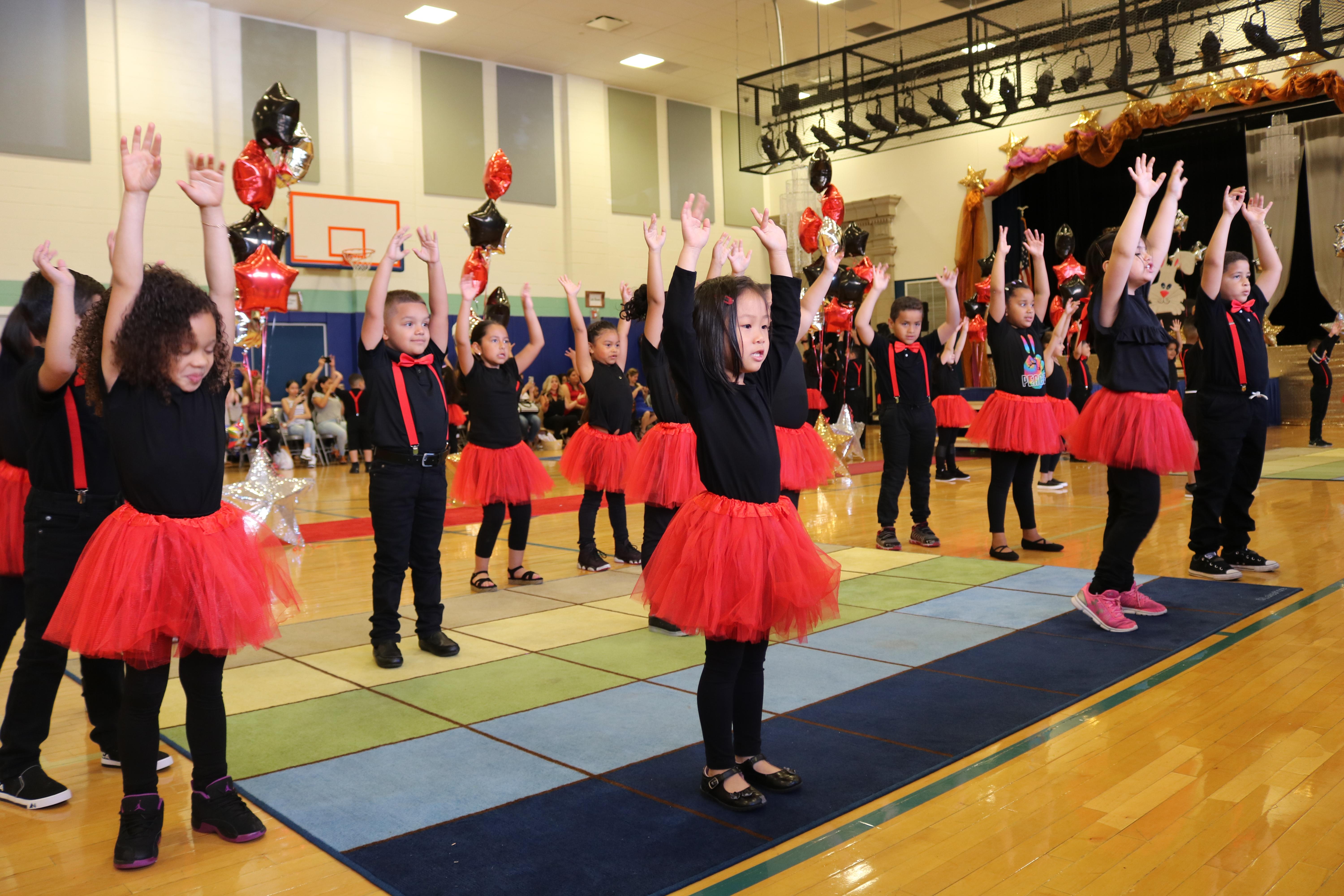 group of kindergarten kids singing with their hands up in the air