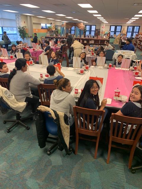family seated at tables in the media center getting ready to paint
